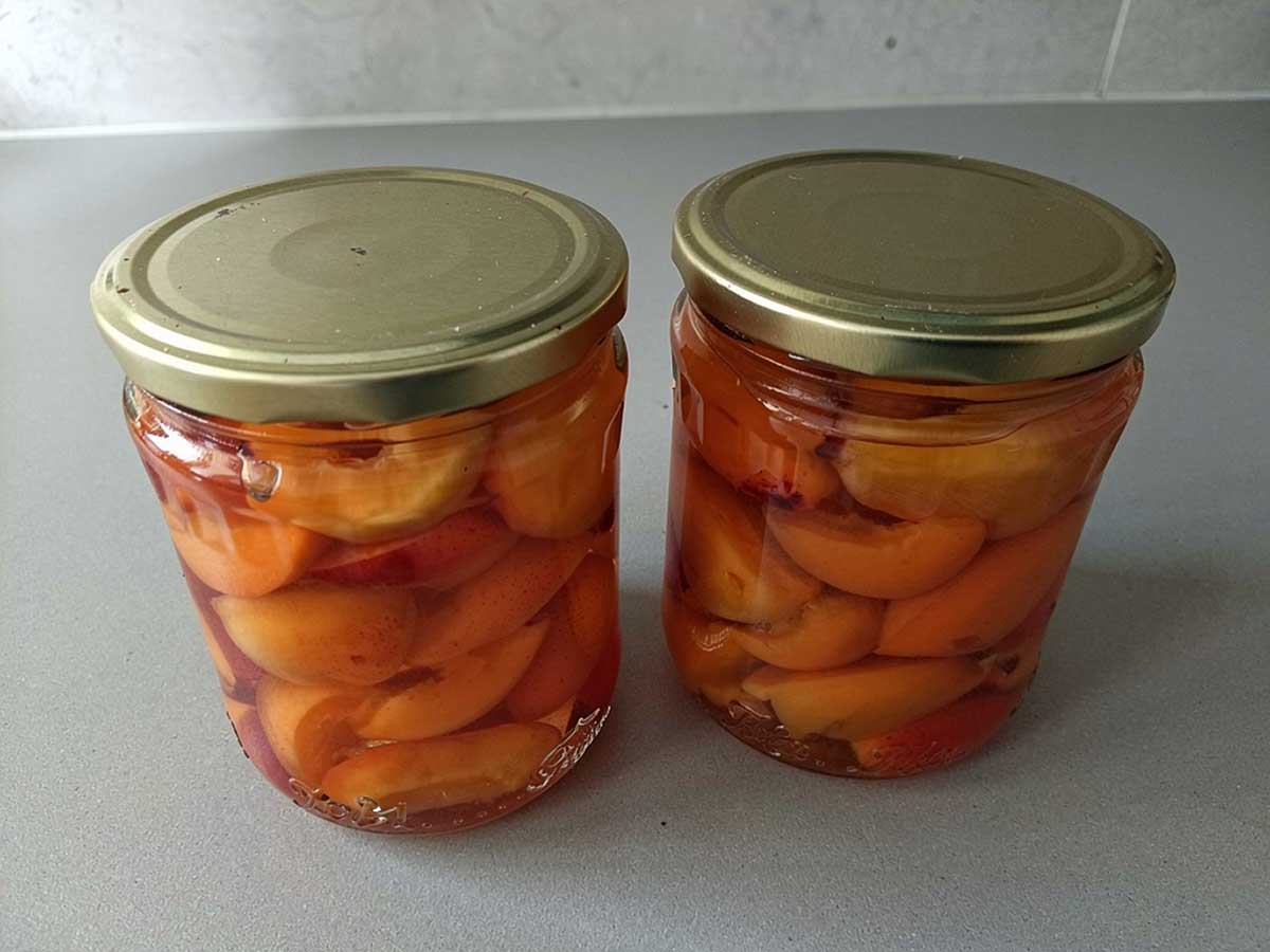 2 inmaakpotten helemaal gevuld met ingemaakte abrikozen in een suikersiroop.