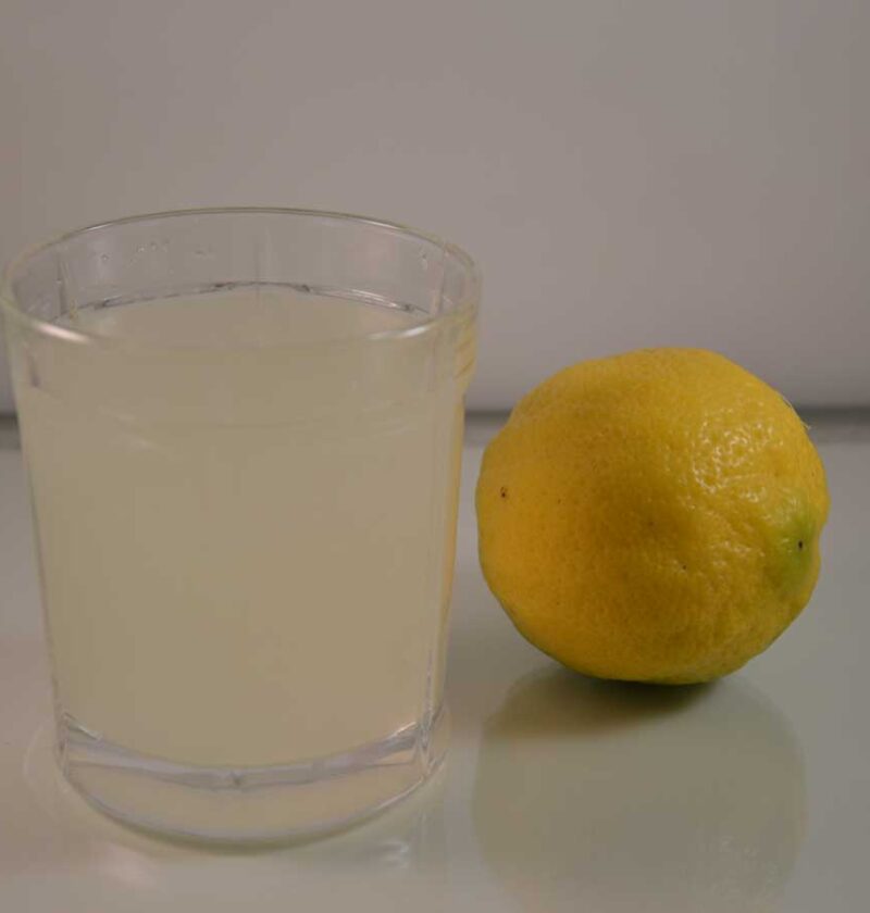 Een glas verse citroenlimonade naast een grote citroen.
