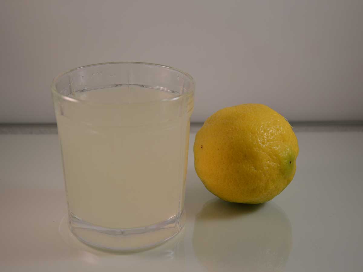 Een glas verse citroenlimonade naast een grote citroen.