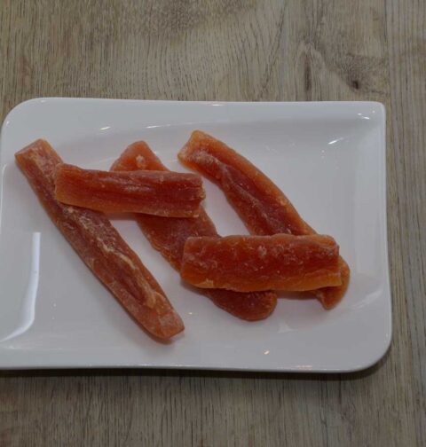 5 stukjes gekonfitje papaja liggen op een wit plat schaaltje.