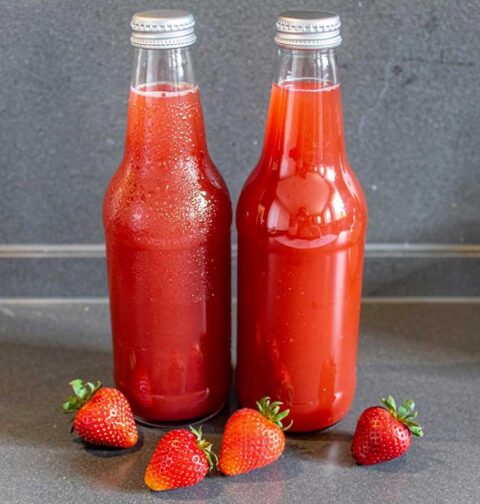 2 flesjes zelfgemaakte aardbeien limonade met wat verse aardbeien.