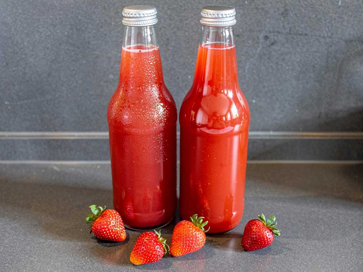2 flesjes zelfgemaakte aardbeien limonade met wat verse aardbeien.