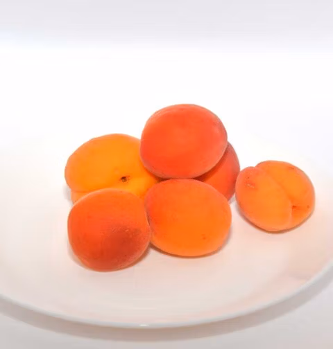 6 Abrikozen op een wit schaaltje, om sap van te maken.