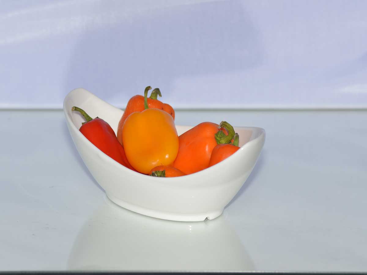 Een wit schaaltje met verse paprika, rood, geel, en oranje.