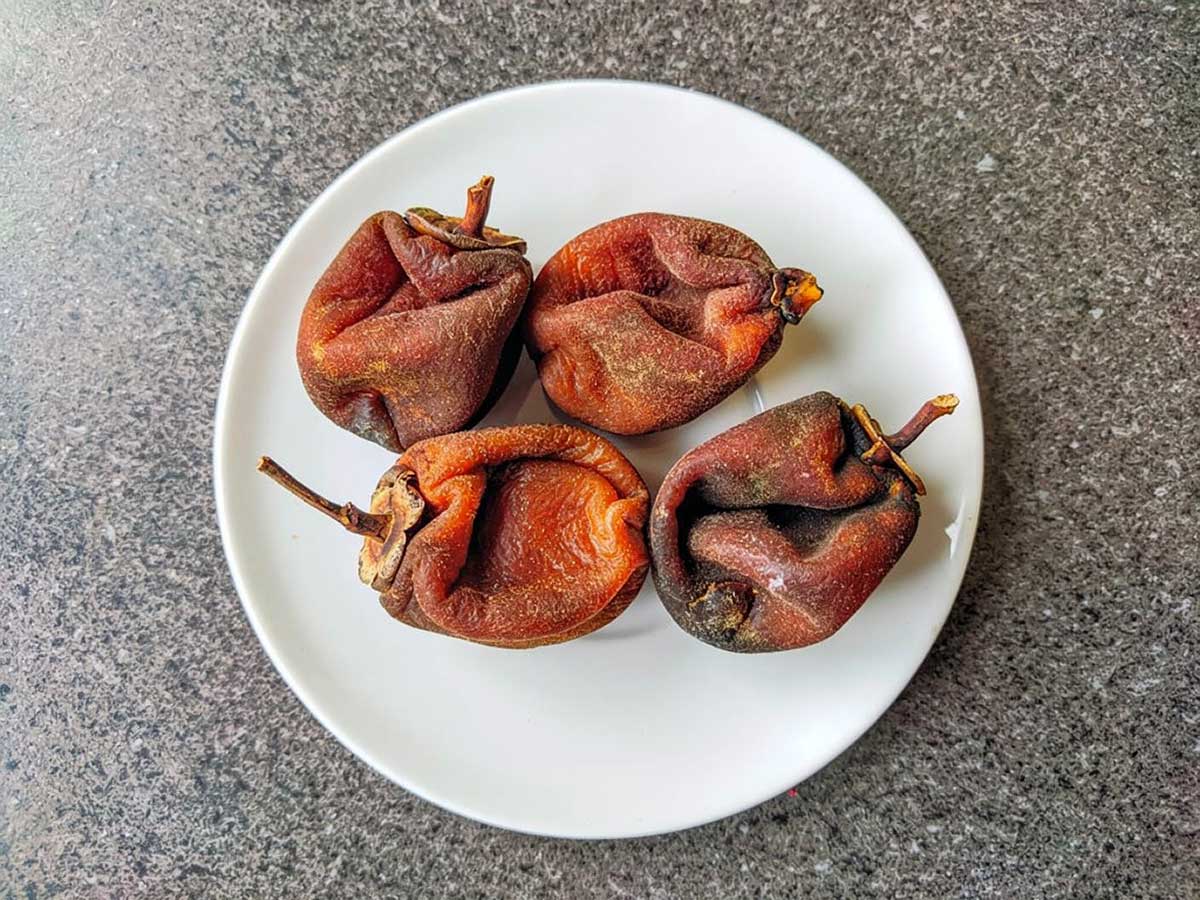 4 gedroogde hele kaki op een wit bord.