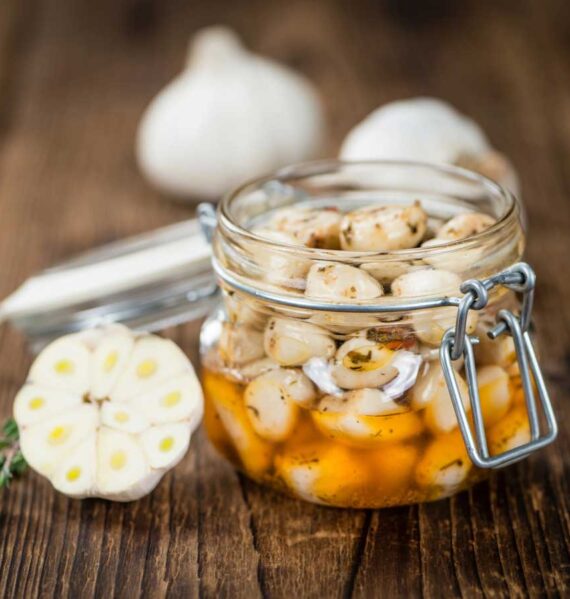 In open inmaakpot met daarin teentjes knoflook, met verse knoflook ernaast.