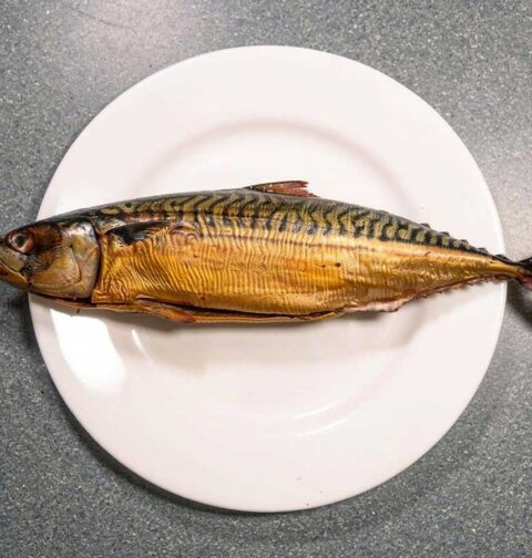 Een hele gerookte makreel op een wit bord.