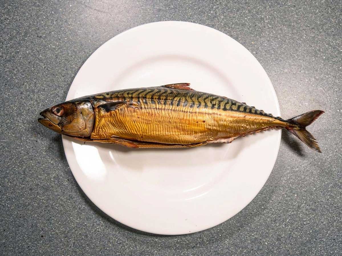 Een hele gerookte makreel op een wit bord.