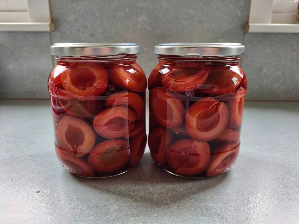 2 grote inmaakpotten met daarin halve ingemaakte pruimen.