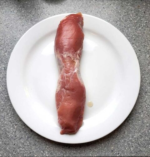 Een hele varkenshaas op een wit bord, ongebakken en klaar om in te vriezen.