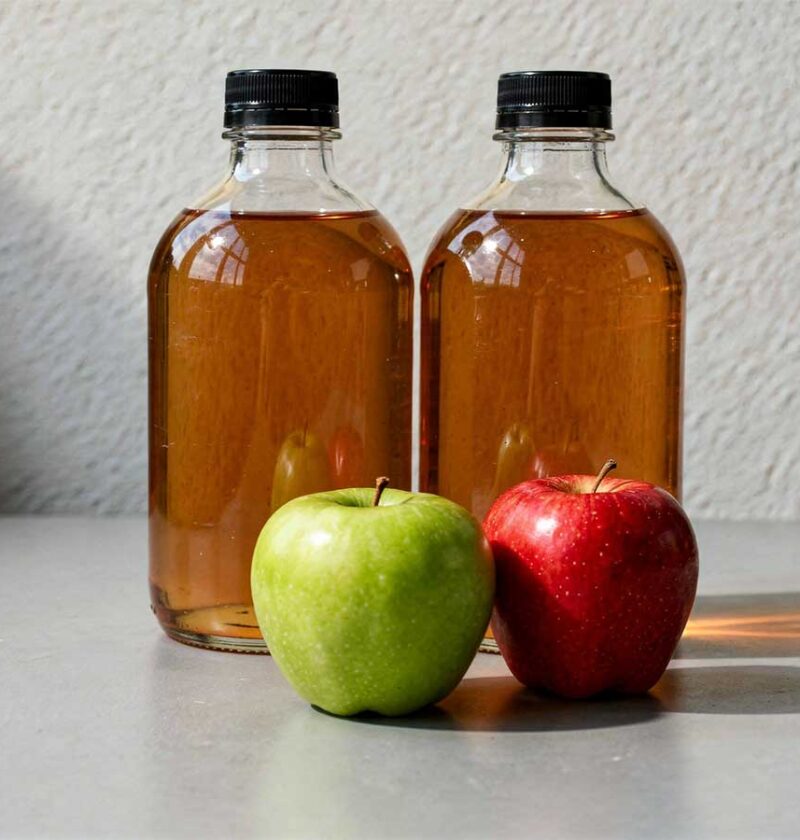 2 flessen appelciderazijn, met daarvoor 2 appels.
