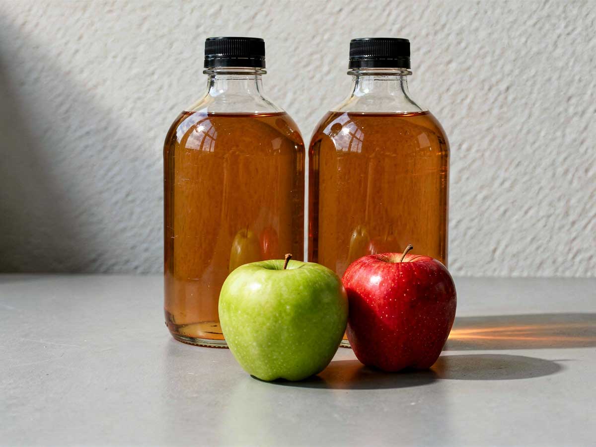 2 flessen appelciderazijn, met daarvoor 2 appels.