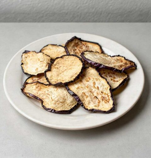 Gedroogde plakjes aubergine op een wit bordje.