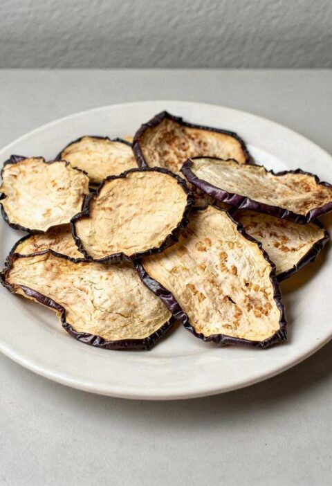 Gedroogde plakjes aubergine op een wit bordje.