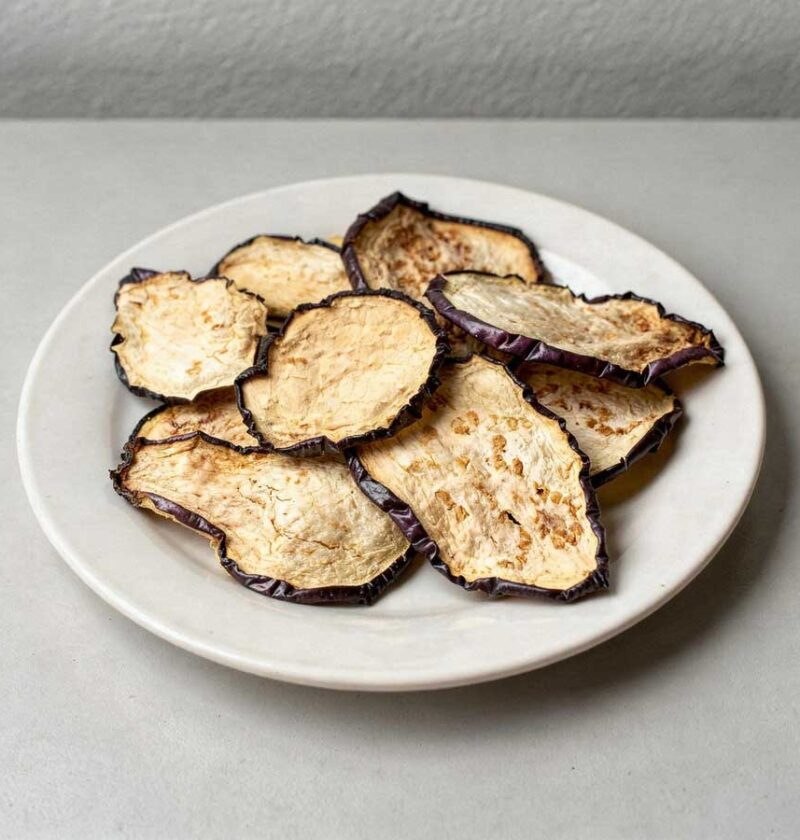Gedroogde plakjes aubergine op een wit bordje.
