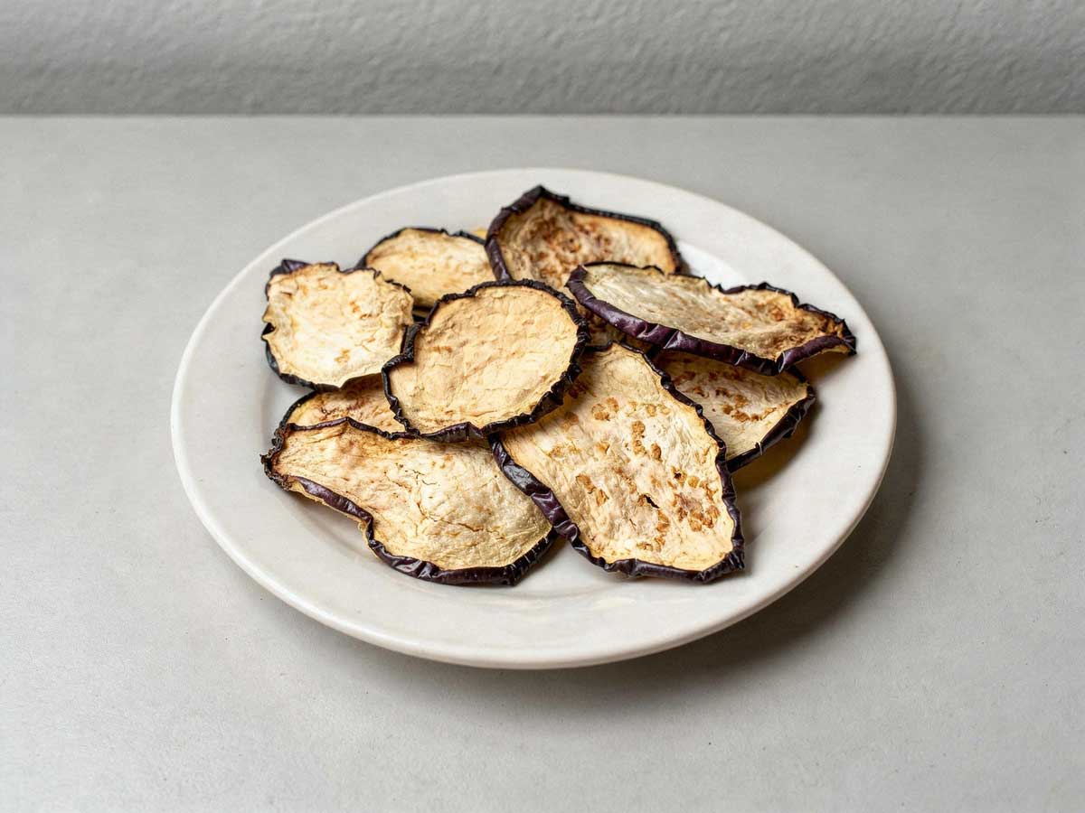 Gedroogde plakjes aubergine op een wit bordje.