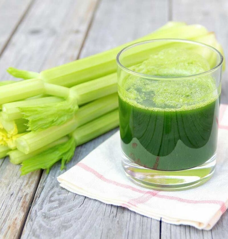 Een glas met bleekselderijsap, naast een verse bleekselderij.