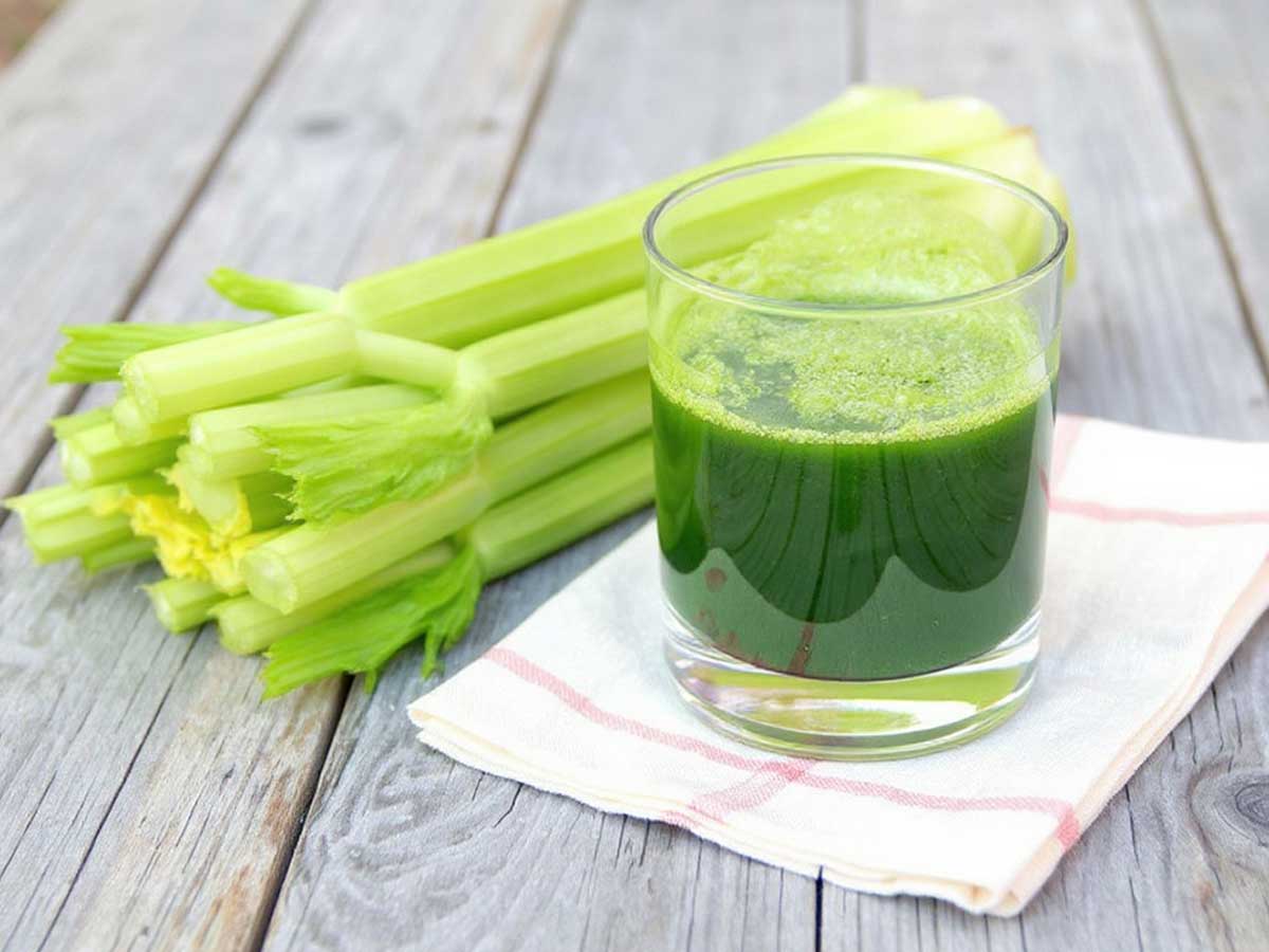 Een glas met bleekselderijsap, naast een verse bleekselderij.