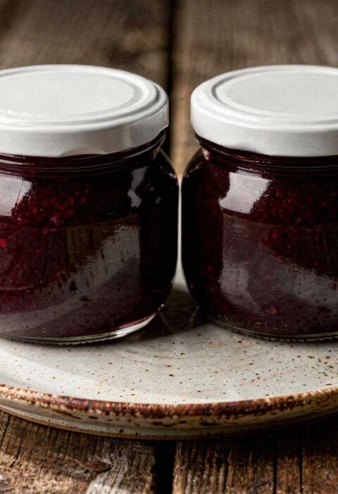 Twee glazen potten met witte deksels vol donkere, zelfgemaakte bramenjam.