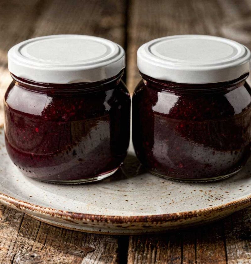 Twee glazen potten met witte deksels vol donkere, zelfgemaakte bramenjam.