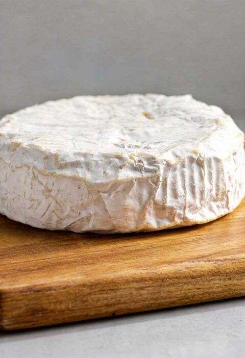 Een hele camembert op een houten snijplank.