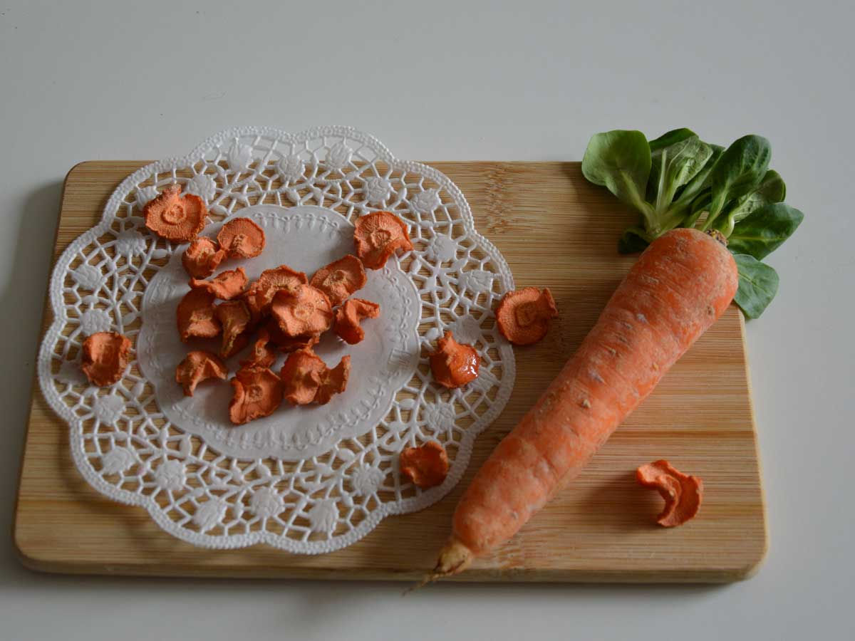 Gedroogde plakjes wortel en een hele winterpeen op een houten snijplank.