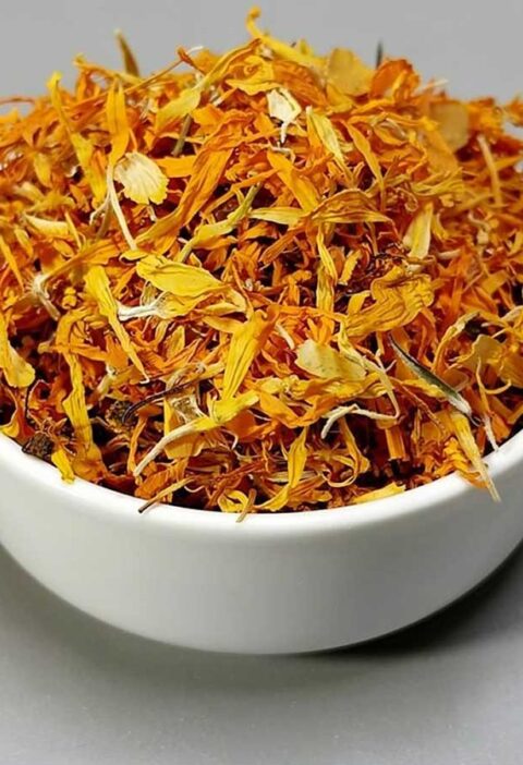 Een wit schaaltje met daarin gedroogde blomeblaadjes van goudsbloemen.