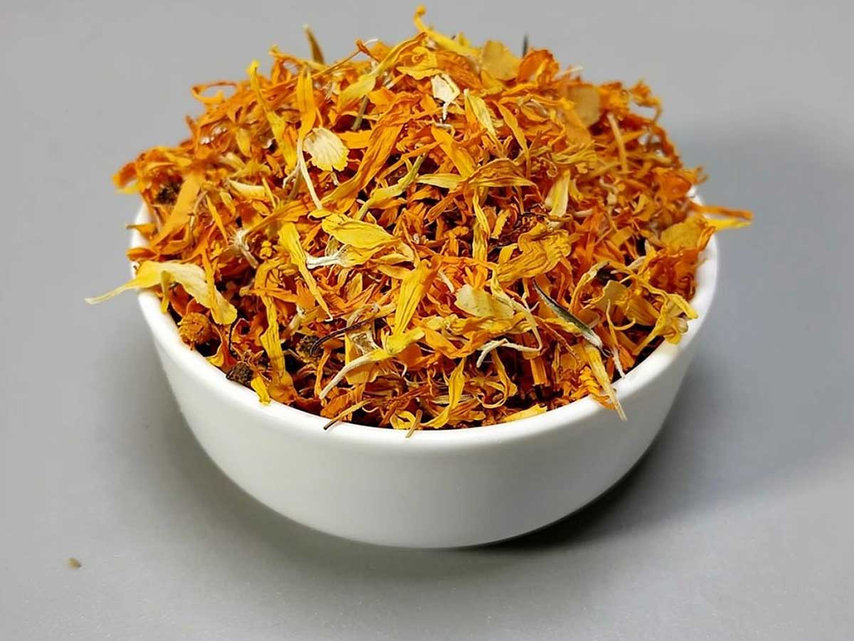 Een wit schaaltje met daarin gedroogde blomeblaadjes van goudsbloemen.
