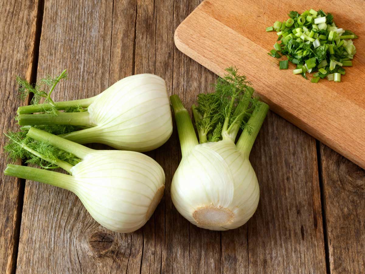 3 venkelknollen naast een snijplank met daarom gesneden bieslook.