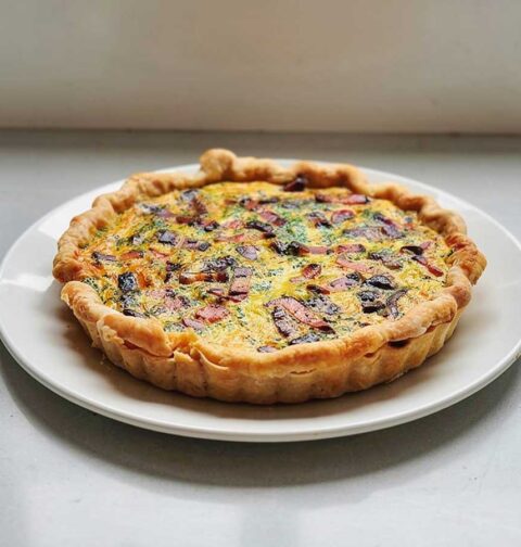 Een hele quiche, uit de vorm, op een wit bord.