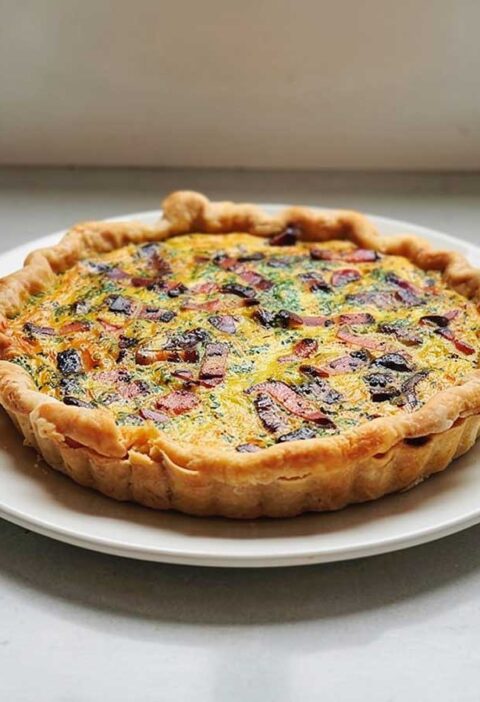 Een hele quiche, uit de vorm, op een wit bord.