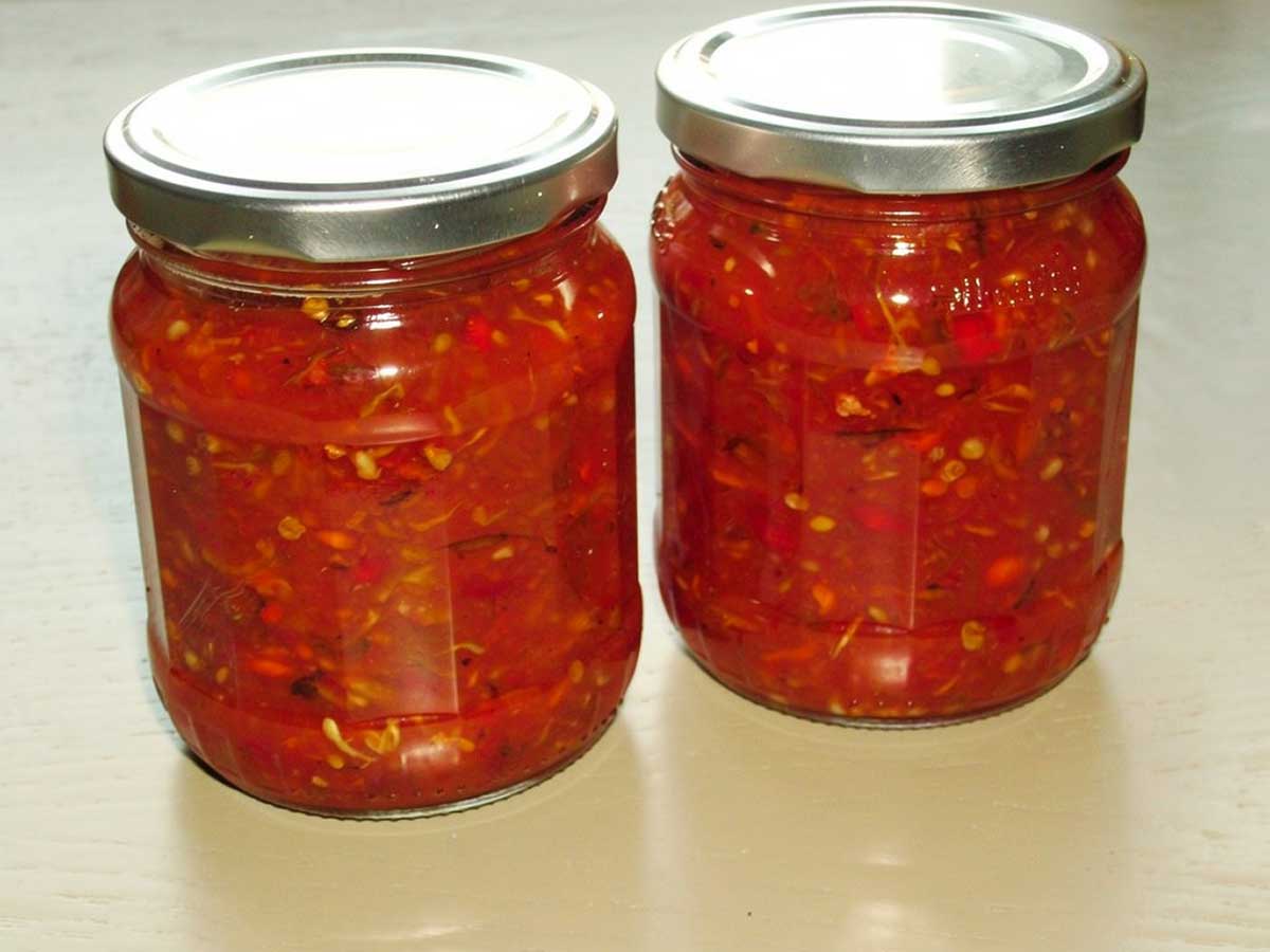 Twee grote potten met daarin zelfgemaakte rode peperjam, met pitjes.