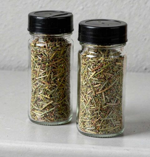 Gedroogde rozemarijnblaadjes in twee kruidenpotjes.