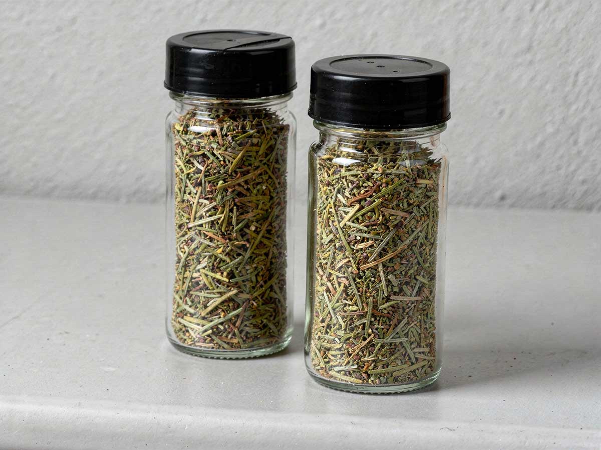 Gedroogde rozemarijnblaadjes in twee kruidenpotjes.