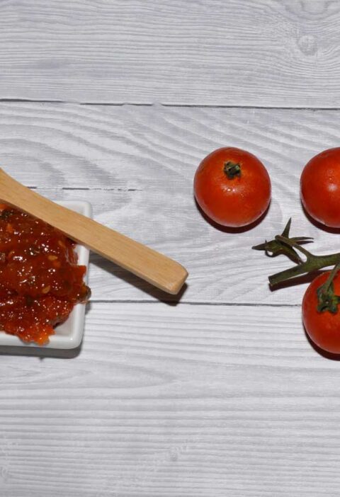 Zelfgemaakte tomatenjam in een klein wit schaaltje, met daarnaast verse tomaten.