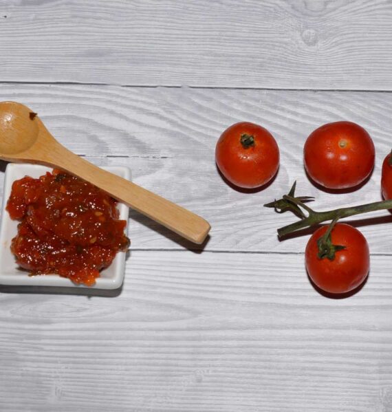 Zelfgemaakte tomatenjam in een klein wit schaaltje, met daarnaast verse tomaten.