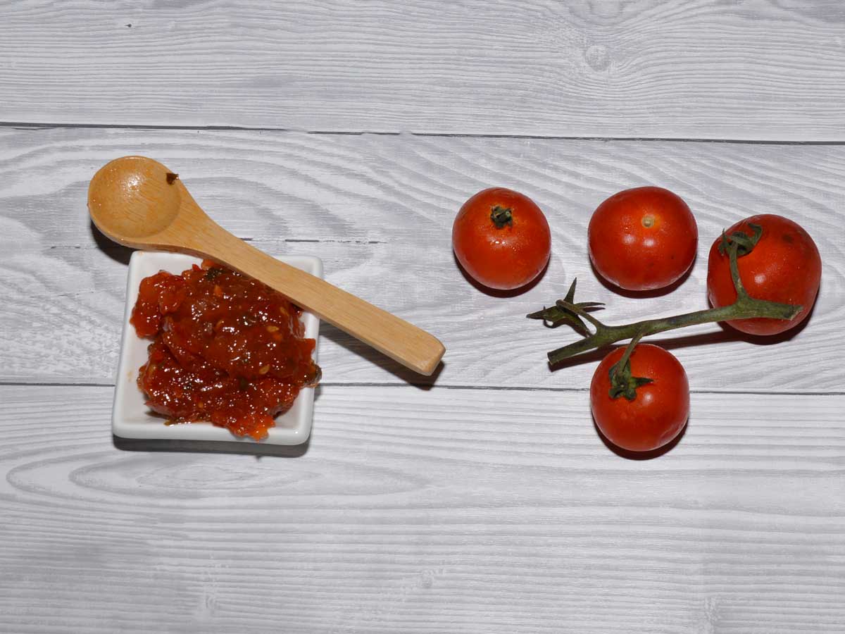 Zelfgemaakte tomatenjam in een klein wit schaaltje, met daarnaast verse tomaten.