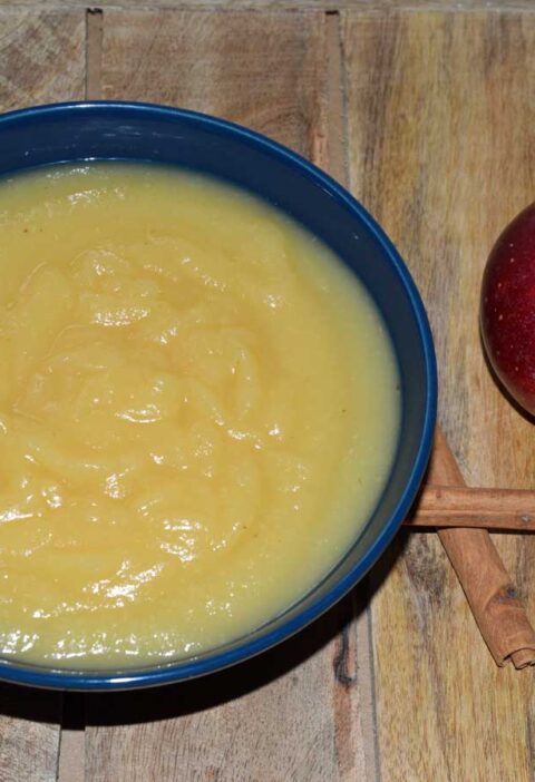 Schaaltje zelfgemaakte appelmoes met daarnaast kaneelstok en appel, klaar om te wecken.