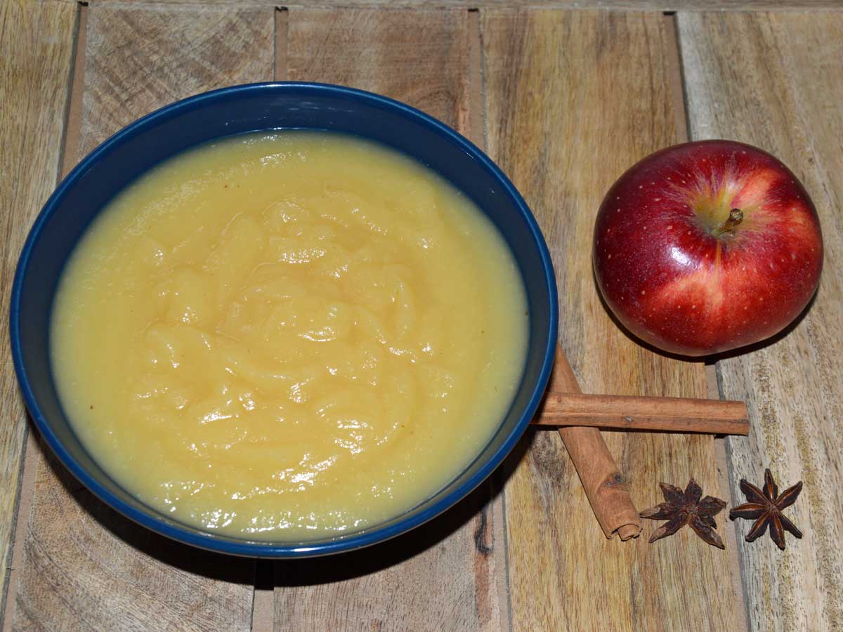 Schaaltje zelfgemaakte appelmoes met daarnaast kaneelstok en appel, klaar om te wecken.