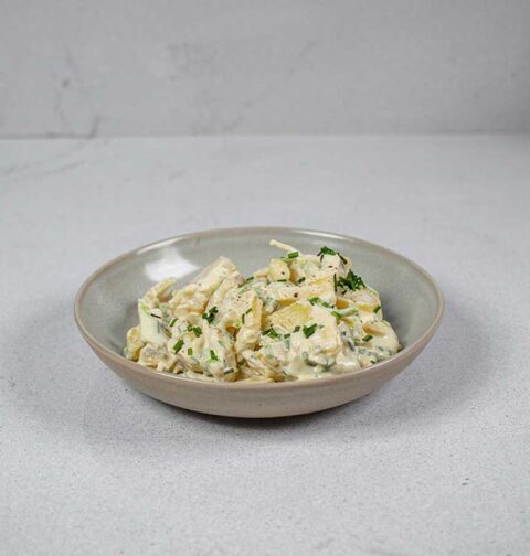 Een schaaltje met aardappelsalade met daarover wat gehakte bieslook.
