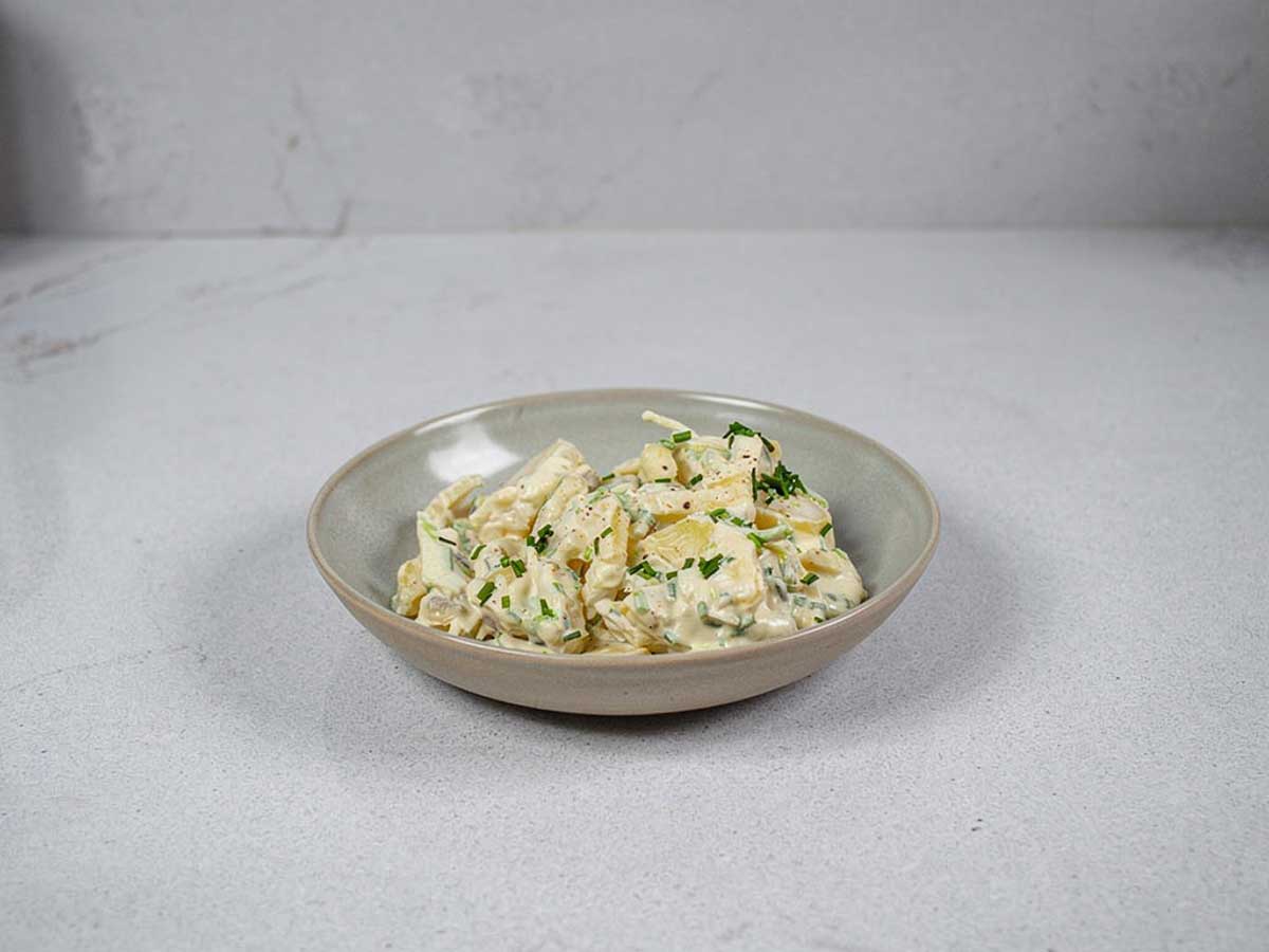 Een schaaltje met aardappelsalade met daarover wat gehakte bieslook.