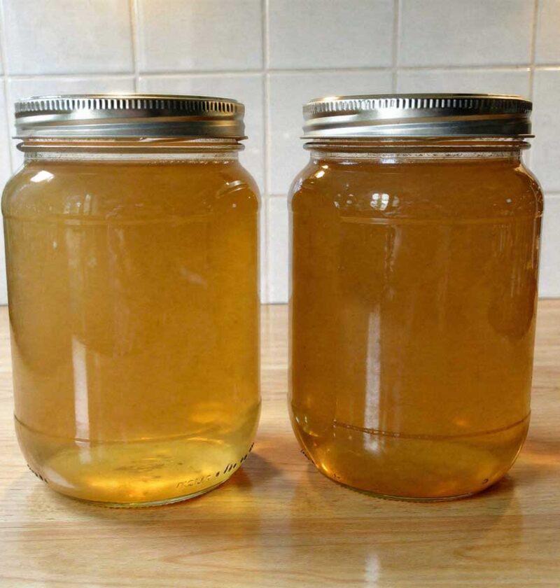 Twee grote glazen weckpotten met schroefdeksel gevuld met verse, heldere bouillon.