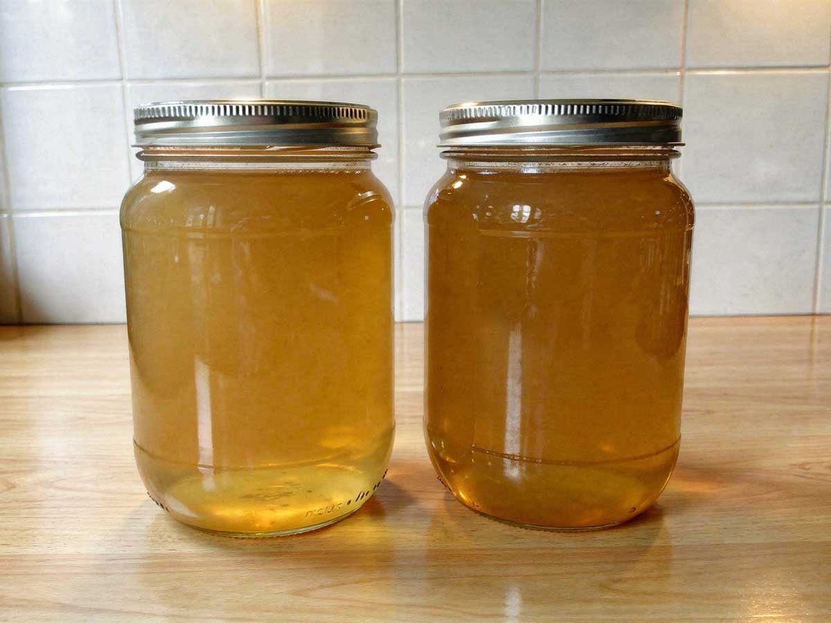 Twee grote glazen weckpotten met schroefdeksel gevuld met verse, heldere bouillon.