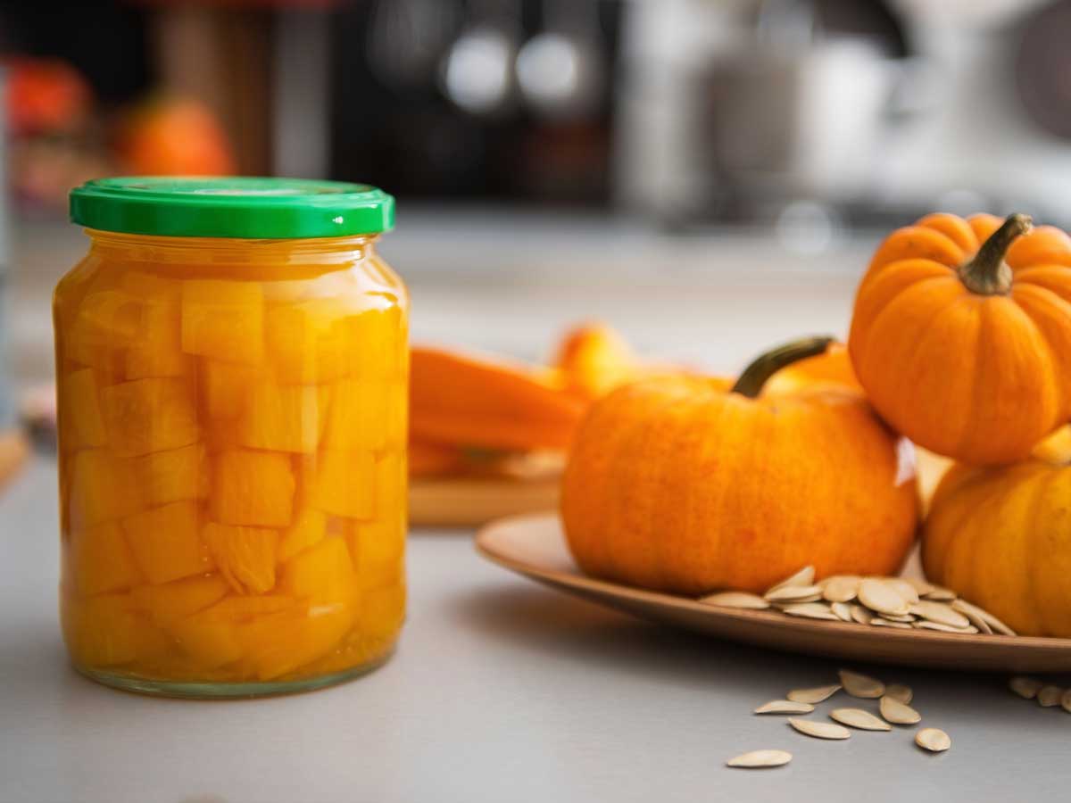 Ingemaakte pompoen naast een schaal met verse pompoenen.