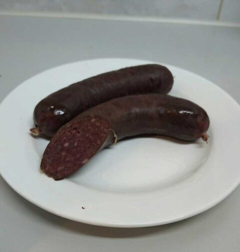 een hele en een aangesneden bloedworst op een bord.