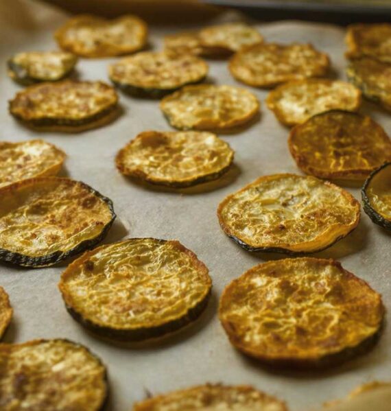 Een met bakpapier beklede bakplaat met daarop gedroogde plakjes courgette.