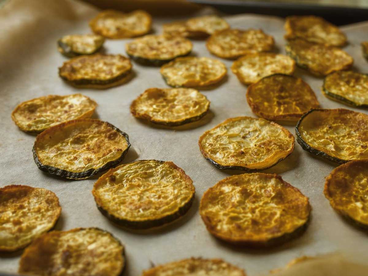 Een met bakpapier beklede bakplaat met daarop gedroogde plakjes courgette.